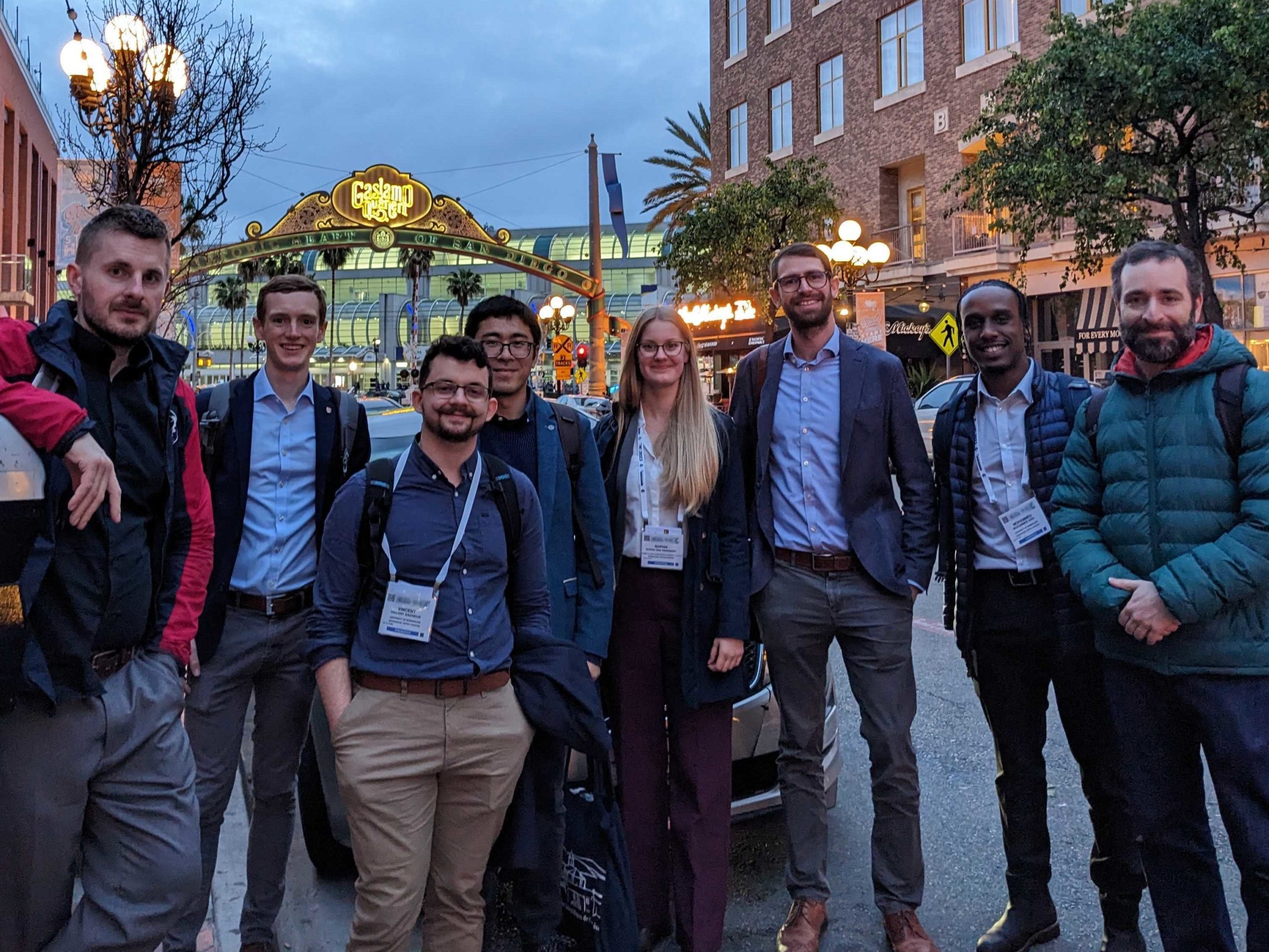 From left to right: Neal Parkes, Tom Blackburn, Vincent Gagneur, Kan Ma, Sophia von Tiedemann, Sandy Knowles, Mohammed Said, Pedro Ferreiros standing in front of Gaslamp Quarter Historic District arch. 
