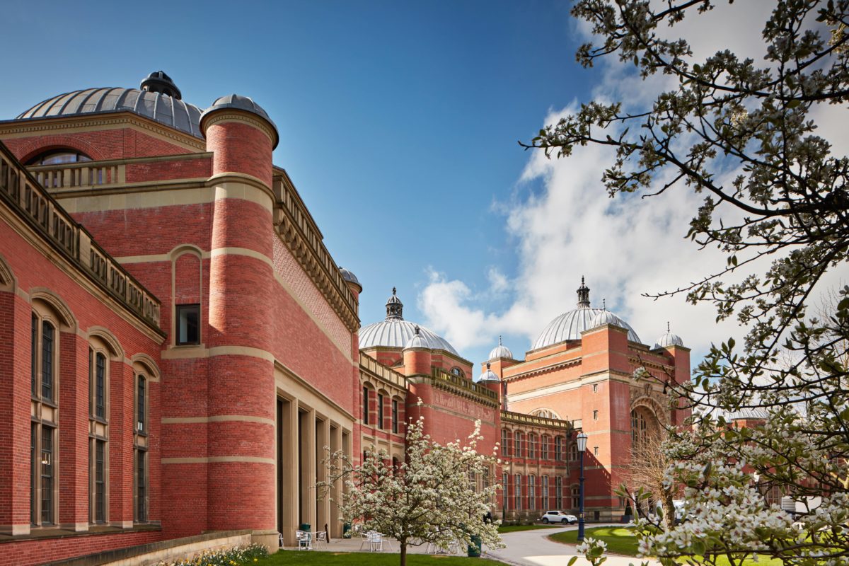 A landscape photograph of the red-bricked Aston Webb building shown from the right. In front are trees with cream-coloured blossom.