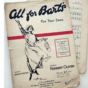 A photograph of two sheet music pages from the “All for Bart’s Fox Trot Song.” The cover page shows a drawing of a nurse with one hand raised in a triumphant gesture, and holding a small bucket in which to collect donations with the other. Text on the cover page states that “Proceeds of the sale of this Fox-Trot go to the funds of St Bartholomew’s Hospital”.