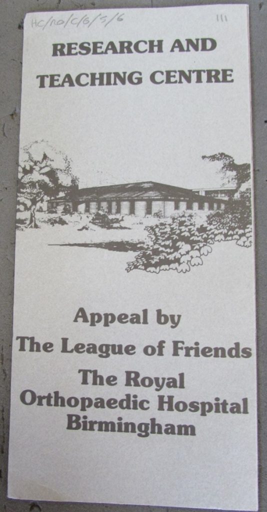 A photograph of the front of a leaflet. The middle of the leaflet has a black and white drawing of a building surrounded by trees and bushes. Above this, in bold grey text, reads "Research And Teaching Centre". Below the drawing, in bold grey text, reads "Appeal by The League of Friends; The Royal Orthopaedic Hospital Birmingham". At the top left of the page, in faint pencil, is the archive reference.