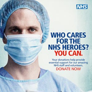 A reproduction of a fundraising appeal poster from NHS Charities Together. The poster features the photograph of a male medical professional wearing personal protective equipment (PPE) including a face mask, a hair net, and blue rubber gloves. The text on the poster says: “Who cares for the heroes? You can. Your donations help provide essential support for our amazing NHS staff and volunteers. Donate Now.” The words donate now are in capital letters. The bottom right of the poster includes the logos of NHS Charities Together and their Covid-19 Urgent Appeal.