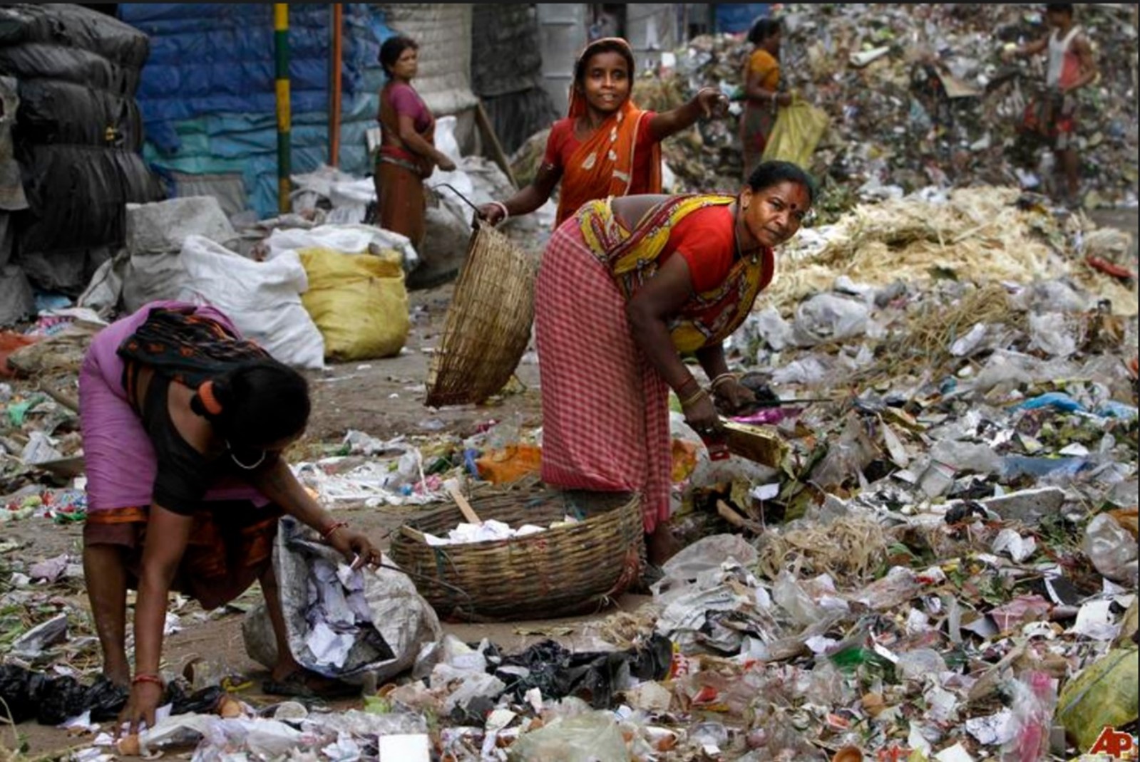 A number of women wearing saris, collecting waste in the middle of a landfill