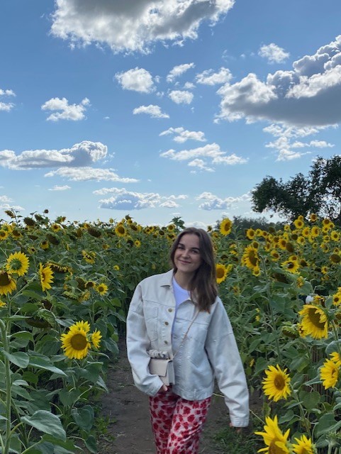 A young woman walks through a field of sunflowers