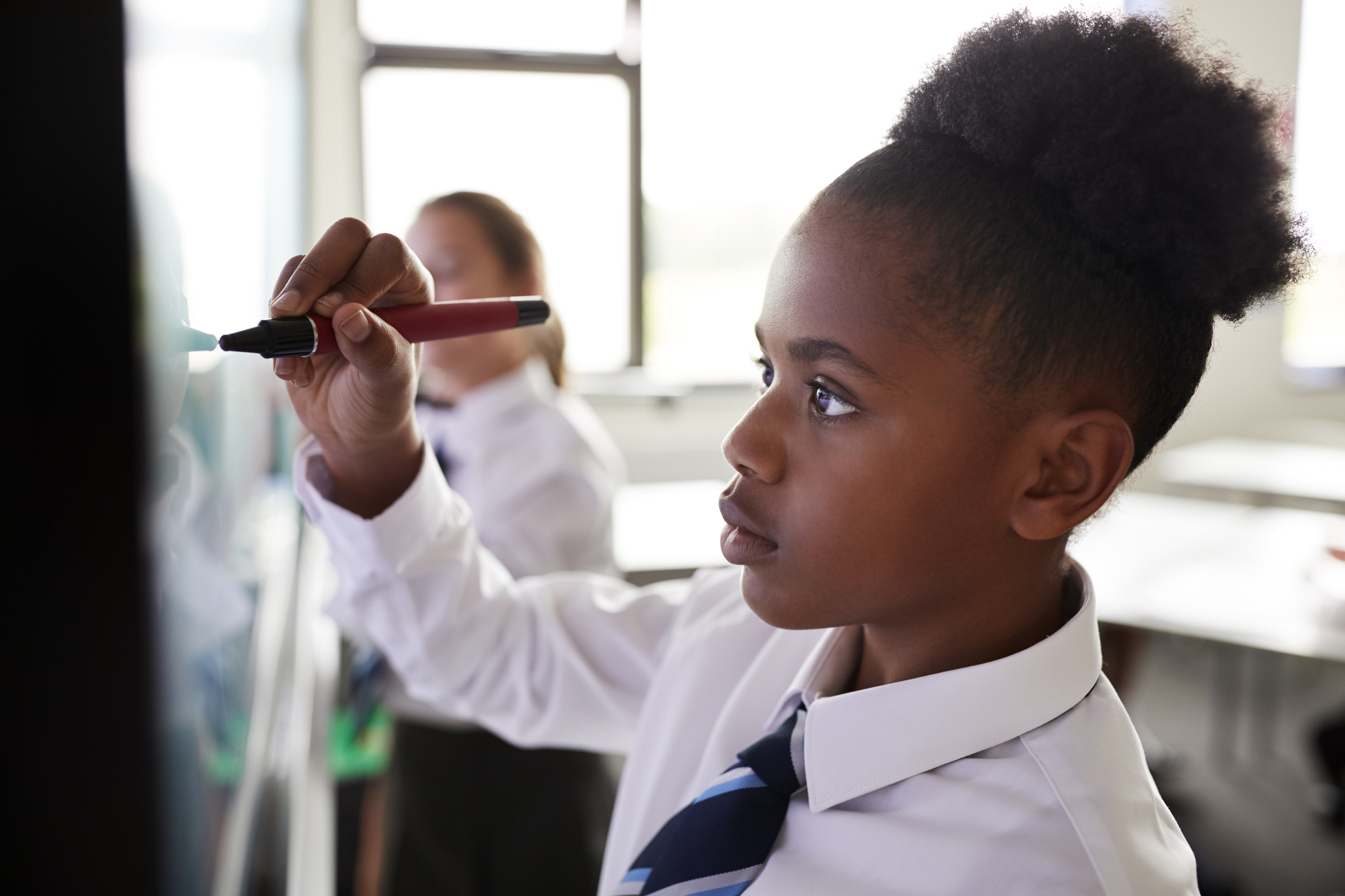 A schoolgirl in uniform writes on a whiteboard