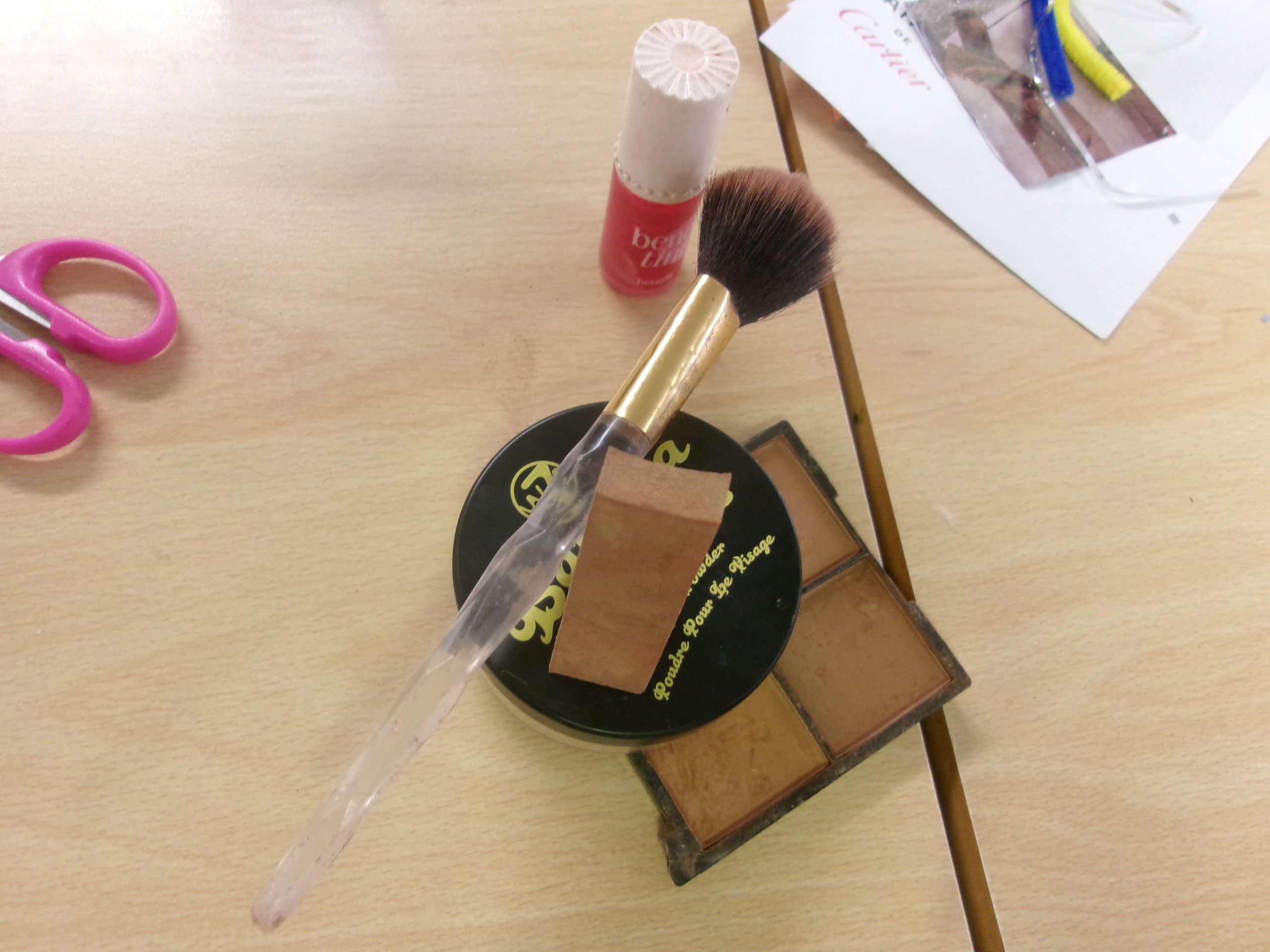 An image of a make-up brush, sponge and powder on a classroom desk.