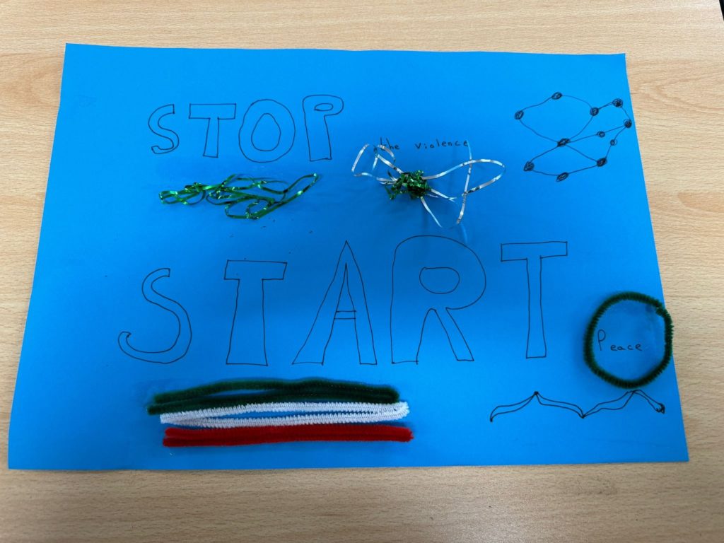 A collage on blue poster paper with the word STOP the violence and START Peace written in marker. These words are emphasised with ribbon and pipe cleaner.